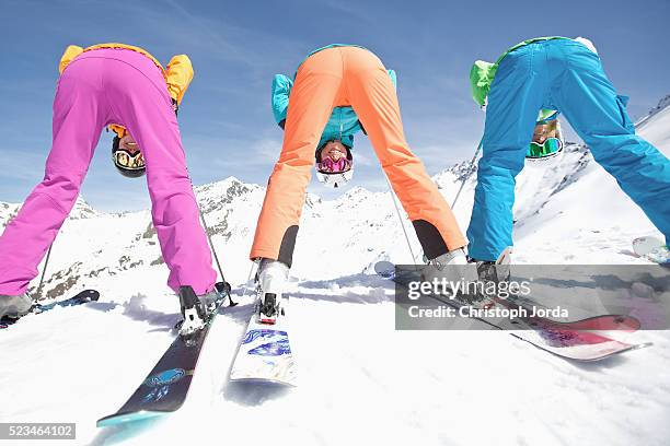 three young female skiers looking through their legs to camera - funny snow skiing fotografías e imágenes de stock