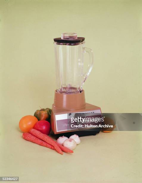 Waring Futura 850 blender sits amid fruits and vegetables against a yellowish background, 1970s.