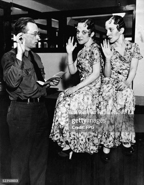 American immigration inspector John J. Conner administers an oath to British co-joined twins Violet Hilton and Daisy Hilton , in matching...