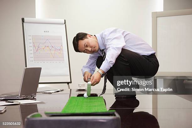 businessman lining up putt in conference room - putting indoors stock pictures, royalty-free photos & images