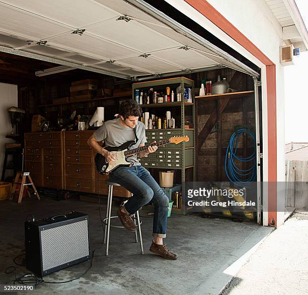 man playing guitar in garage - playing electric guitar stock-fotos und bilder
