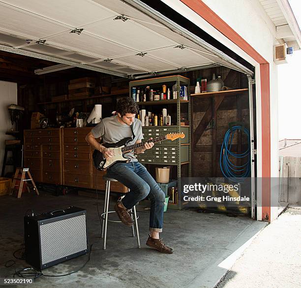 man playing guitar in garage - guitariste photos et images de collection