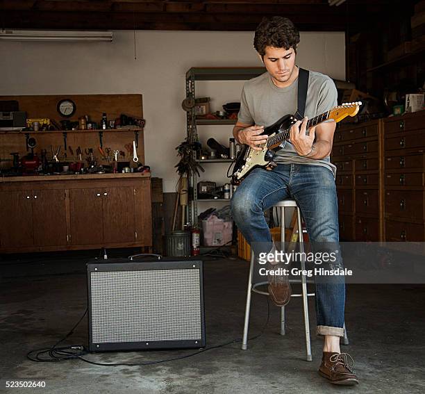 man playing guitar in garage - guitarrista fotografías e imágenes de stock