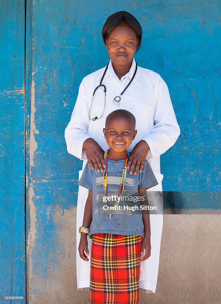 African female doctor and smiling girl (10-12) standing against blue wall