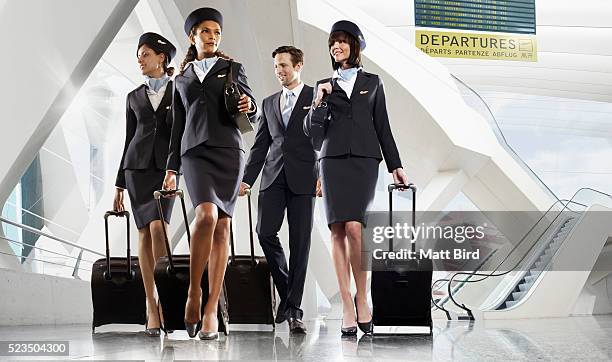 male and female cabin crew walking through large modern airport building - flight attendants stock pictures, royalty-free photos & images