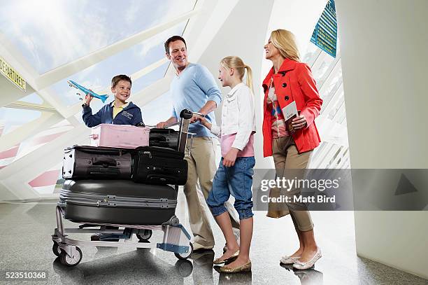 family with two children (10-12, 13-15) pushing trolley through airport - airport family stock-fotos und bilder