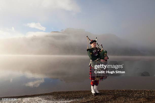 bagpiper playing bagpipes, standing next to scottish loch. west coast scotland - bagpipe stock pictures, royalty-free photos & images