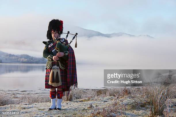 bagpiper playing bagpipes, standing next to scottish loch. west coast scotland - scozia foto e immagini stock