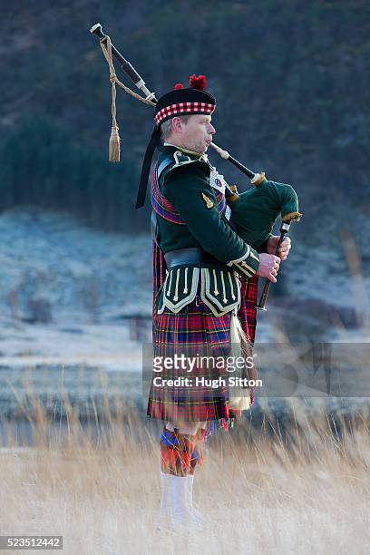 bagpiper playing bagpipes at glenfinnan, next to loch shiel. west coast scotland - bagpipes stock-fotos und bilder