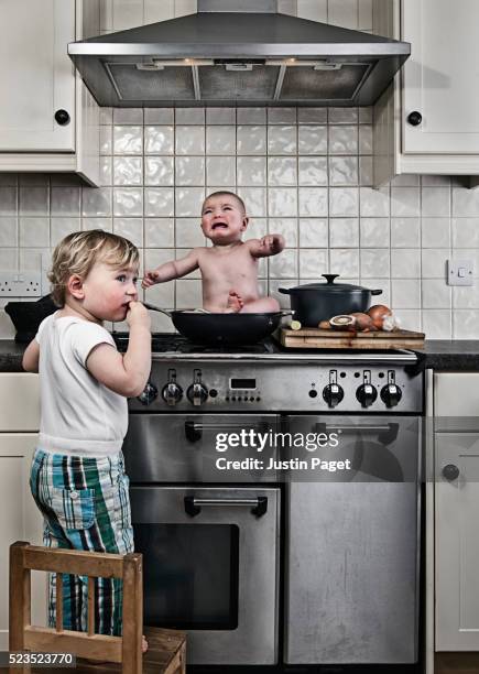 young boy (3-4) caught cooking baby brother (1-6 months) on stove - geschwister frech stock-fotos und bilder