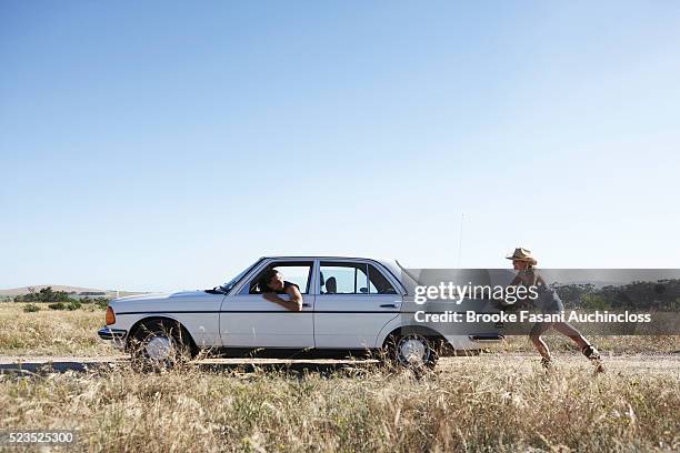 woman pushing car while man drives - geschlechter rollentausch stock-fotos und bilder