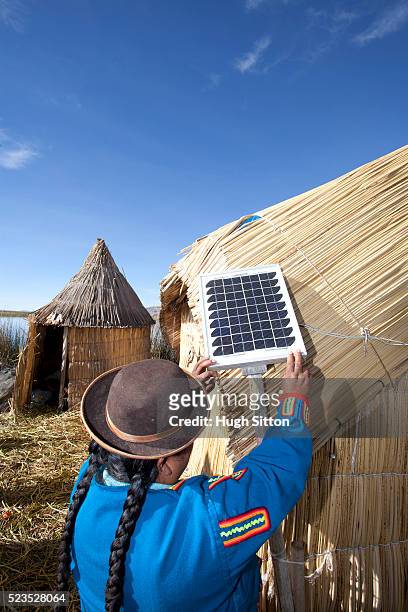 woman wearing traditional costume, using solar panel, on the uros islands of lake titicaca. puno, peru. - zonne eiland stockfoto's en -beelden