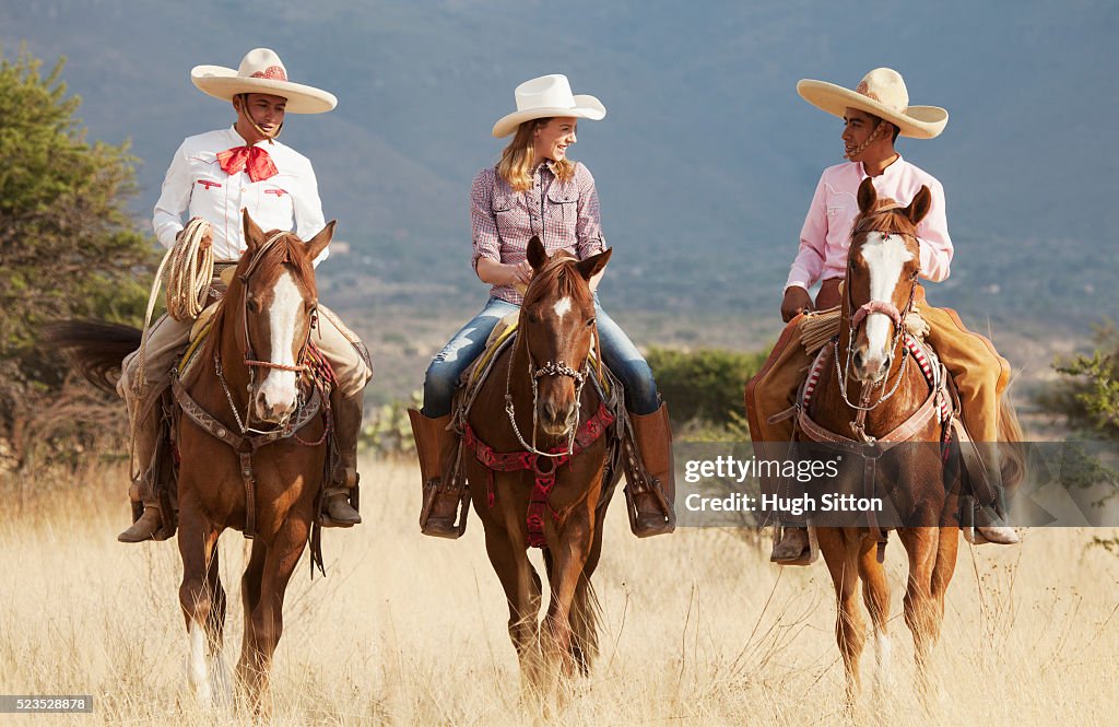 Two cowboys and woman riding horses