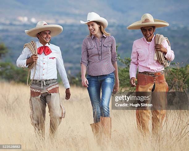 two cowboys and woman walking through field - sombrero hat stockfoto's en -beelden