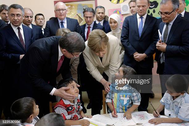 German Chancellor Angela Merkel and Turkish Prime Minister Ahmet Davutoglu talk with refugee children at a preschool, during a visit to a refugee...
