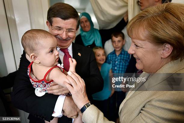 In this photo provided by the German Government Press Office , Turkey's Prime Minister, Ahmet Davutoglu holds a child as German Chancellor Angela...