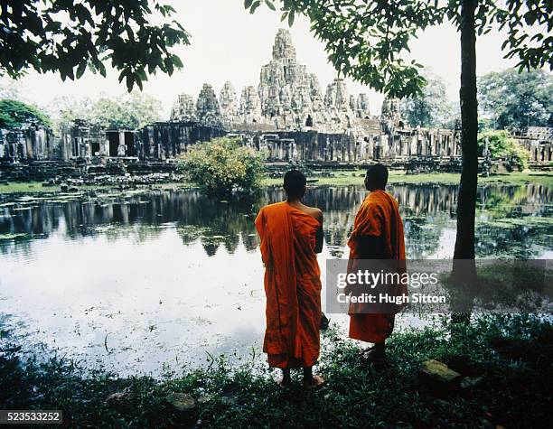 two buddhist monks by lake opposite temple - hugh sitton stock-fotos und bilder