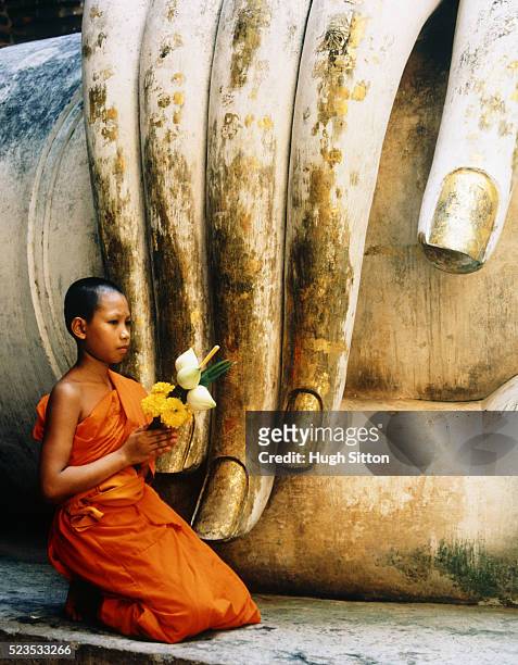 novice buddhist monk kneeling next to fingers of statue - wat si chum stockfoto's en -beelden