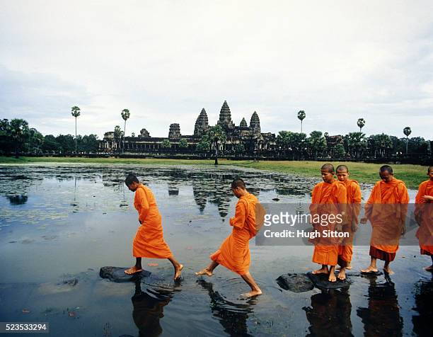 buddhist monks crossing lake on rocks - hugh sitton stock pictures, royalty-free photos & images