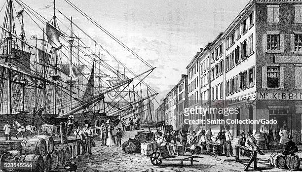 An etching from a painting titled View of South Street, from Maiden Lane, New York City, a line of tall masted ships stands opposite the buildings...