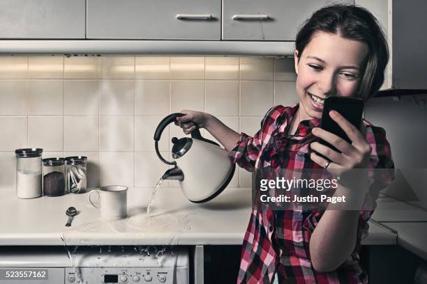 teenage girl on phone whilst pouring kettle - distraído imagens e fotografias de stock