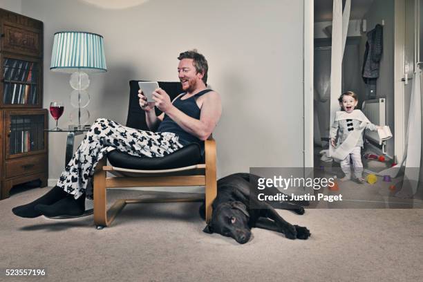 fathers on tablet whilst baby causes chaos - baby animals stock-fotos und bilder