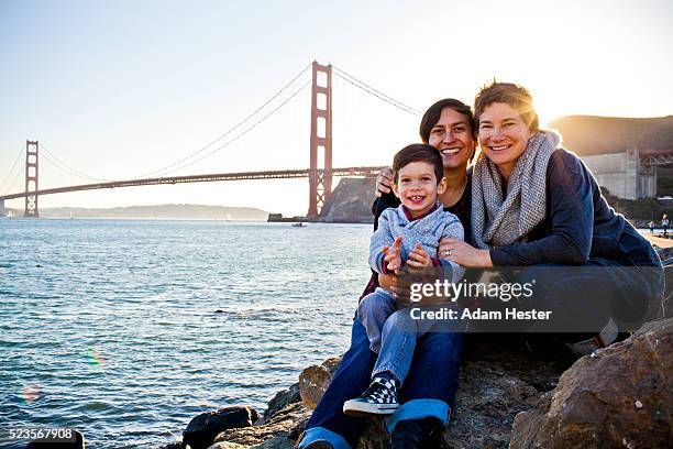 portrait of lesbian family with toddler son (2-3) sitting on shore, san francisco, california, usa - san francisco bay stock pictures, royalty-free photos & images