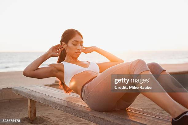 young woman doing sit-ups on bench - sit up foto e immagini stock