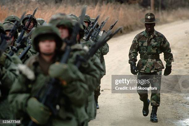 Drill sergeant shepherds a platoon of female trainees in winter gear to the bayonet course during Basic Training at Fort Dix. For a time women were...