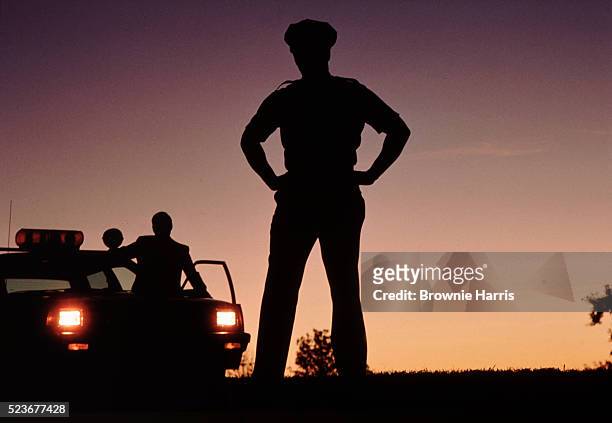 silhouette of policemen with police car in background - cop car photos et images de collection