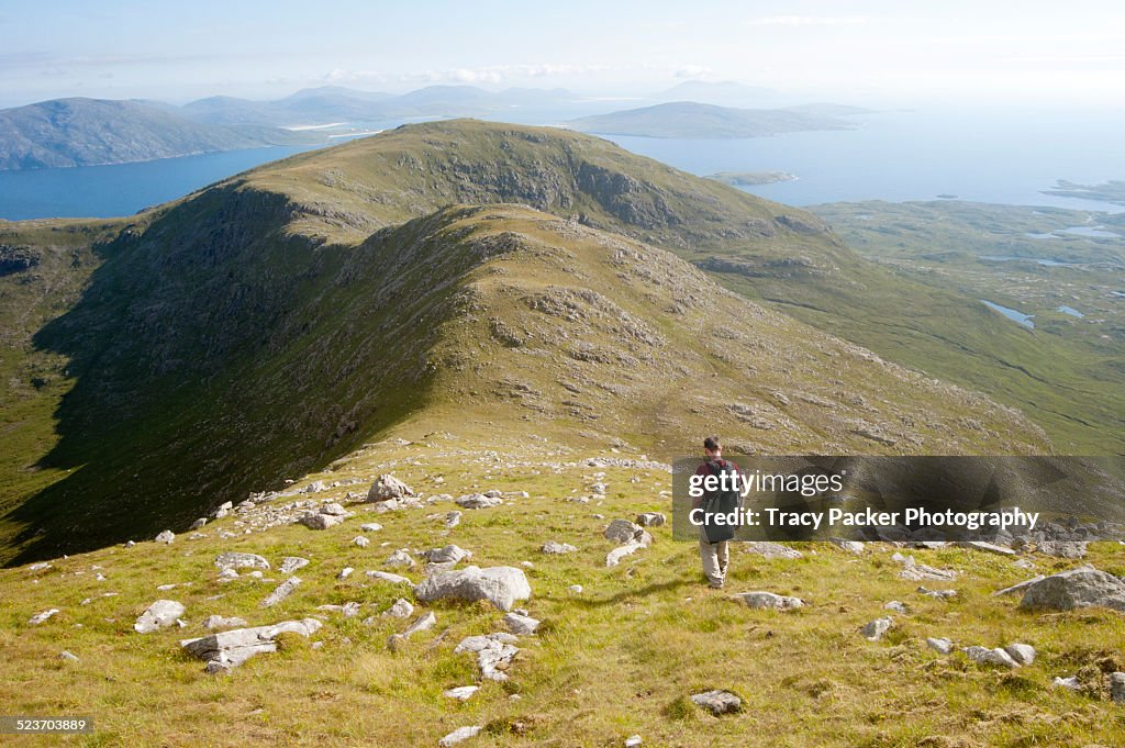 A hiker descends a stony hillside in North Harris