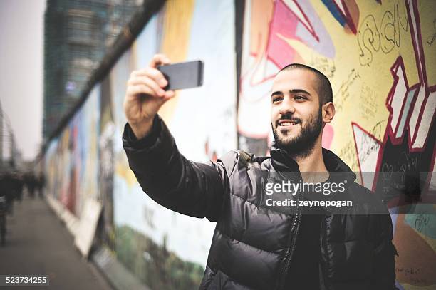 young man taking selfie in front of the berlin wall - photographing graffiti stock pictures, royalty-free photos & images