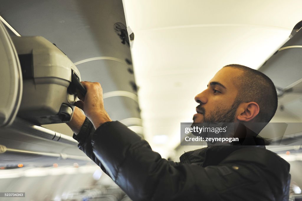 Young man putting a suitcase in an overhead compartment