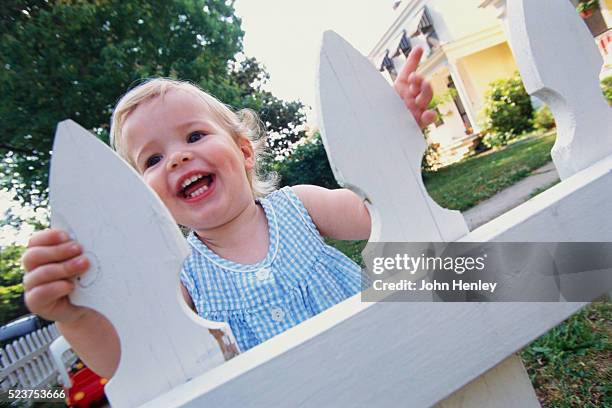 smiling toddler at white picket fence - tuinhek stockfoto's en -beelden