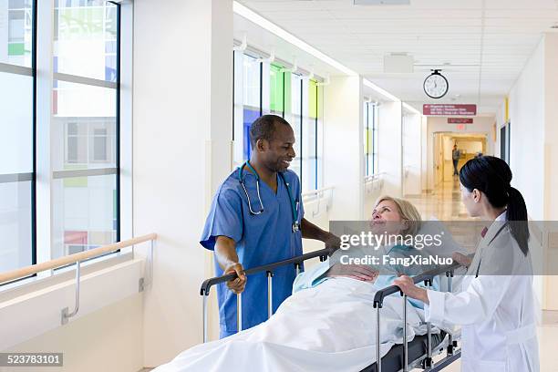 two doctors wheeling patient down hallway - patient lying down stock pictures, royalty-free photos & images