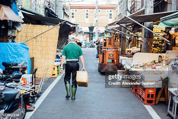man with basket walking among stalls at tsukiji fish market, tokyo, japan - mercato del pesce di tsukiji foto e immagini stock