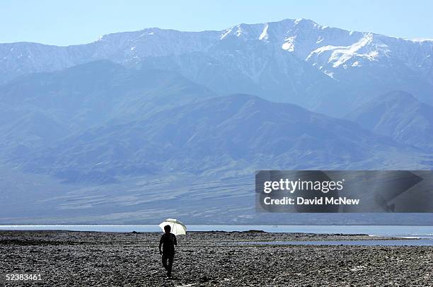 With temperatures already in the mid-90's, a woman walks with a parasol at the edge of a giant lake in the bottom of Death Valley caused by recent...