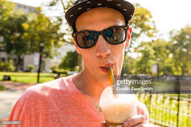 portrait of young man drinking frappe in park - café frappé fotografías e imágenes de stock