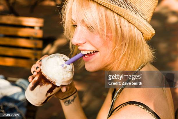 young woman drinking frappe with a straw in park - café frappé fotografías e imágenes de stock