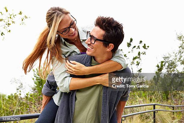 couple playing piggyback ride in park - gafas de ver fotografías e imágenes de stock