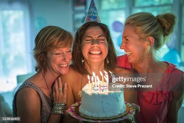 mature woman holding birthday cake, making wish while two friends look on - birthday cake ストックフォトと画像