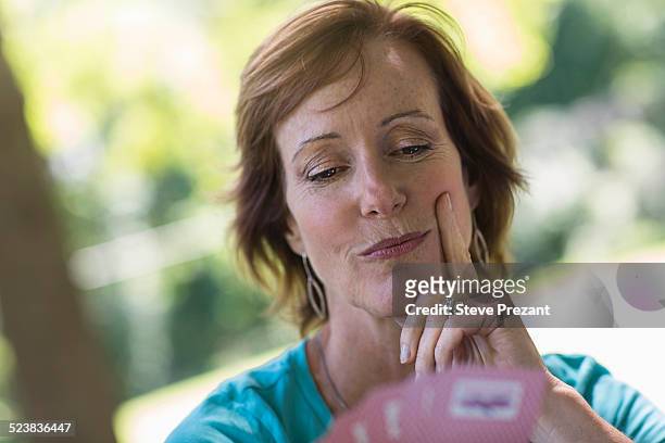 mature woman looking at hand of playing cards - thinking of you card stock-fotos und bilder