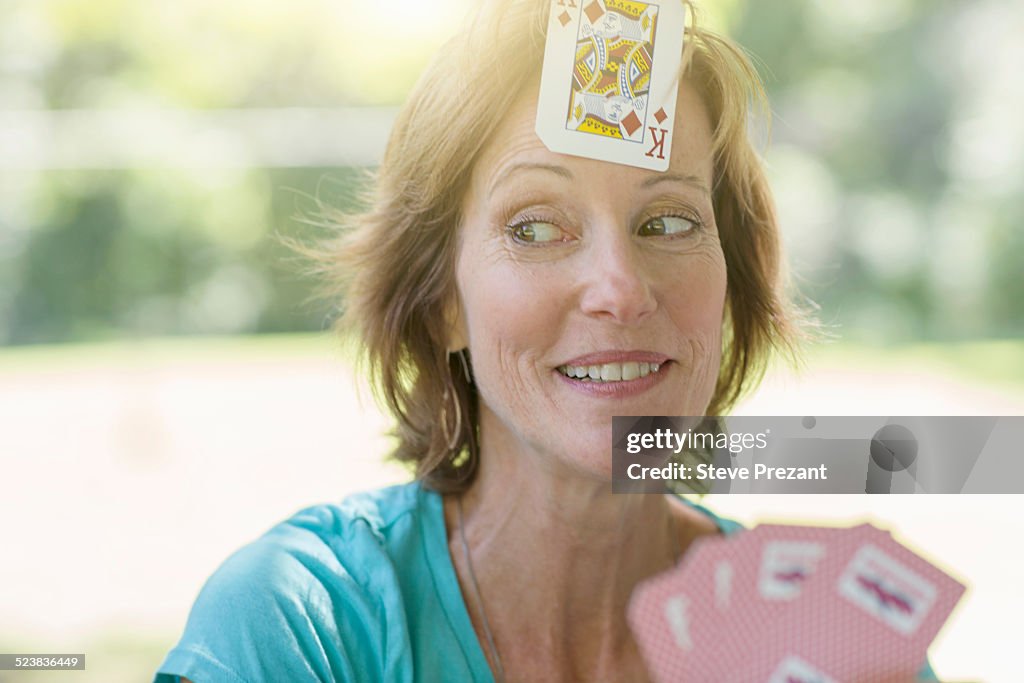 Mature woman playing cards, a playing card stuck on her forehead