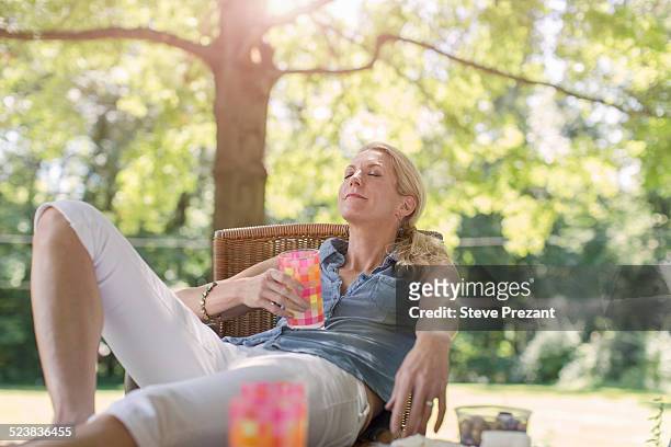 mature woman relaxing in garden with drink - driekwart broek stockfoto's en -beelden