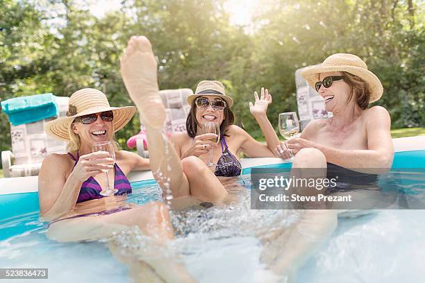 three mature women sitting in paddling pool, drinking wine - wijn tuin stockfoto's en -beelden