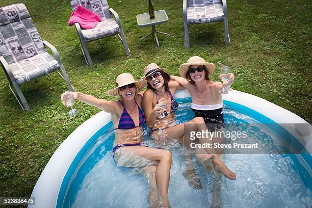 three mature women sitting in paddling pool, drinking wine, elevated view - planschbecken stock-fotos und bilder