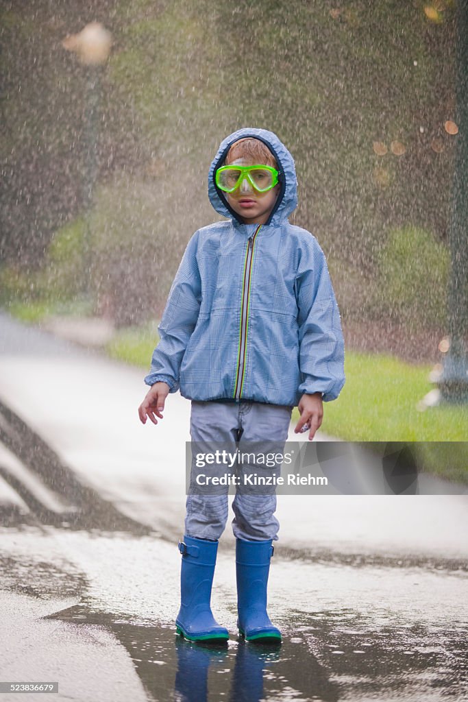 Portrait of boy wearing scuba goggles and rubber boots standing in street puddle