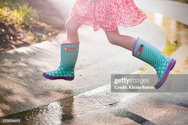 waist down view of girl jumping puddles on rainy street - waterproof photos et images de collection