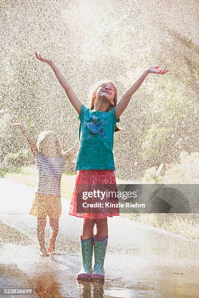 two girls with arms open standing in water spray on street - standing in the rain girl stockfoto's en -beelden