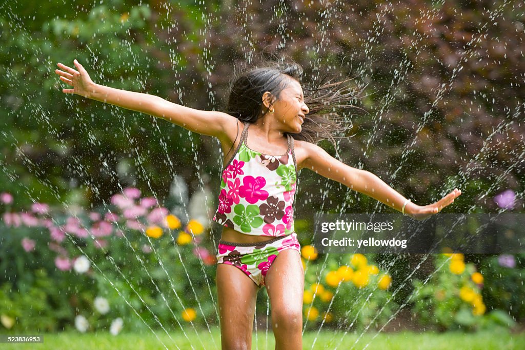 Girl in swimming costume playing with garden sprinkler
